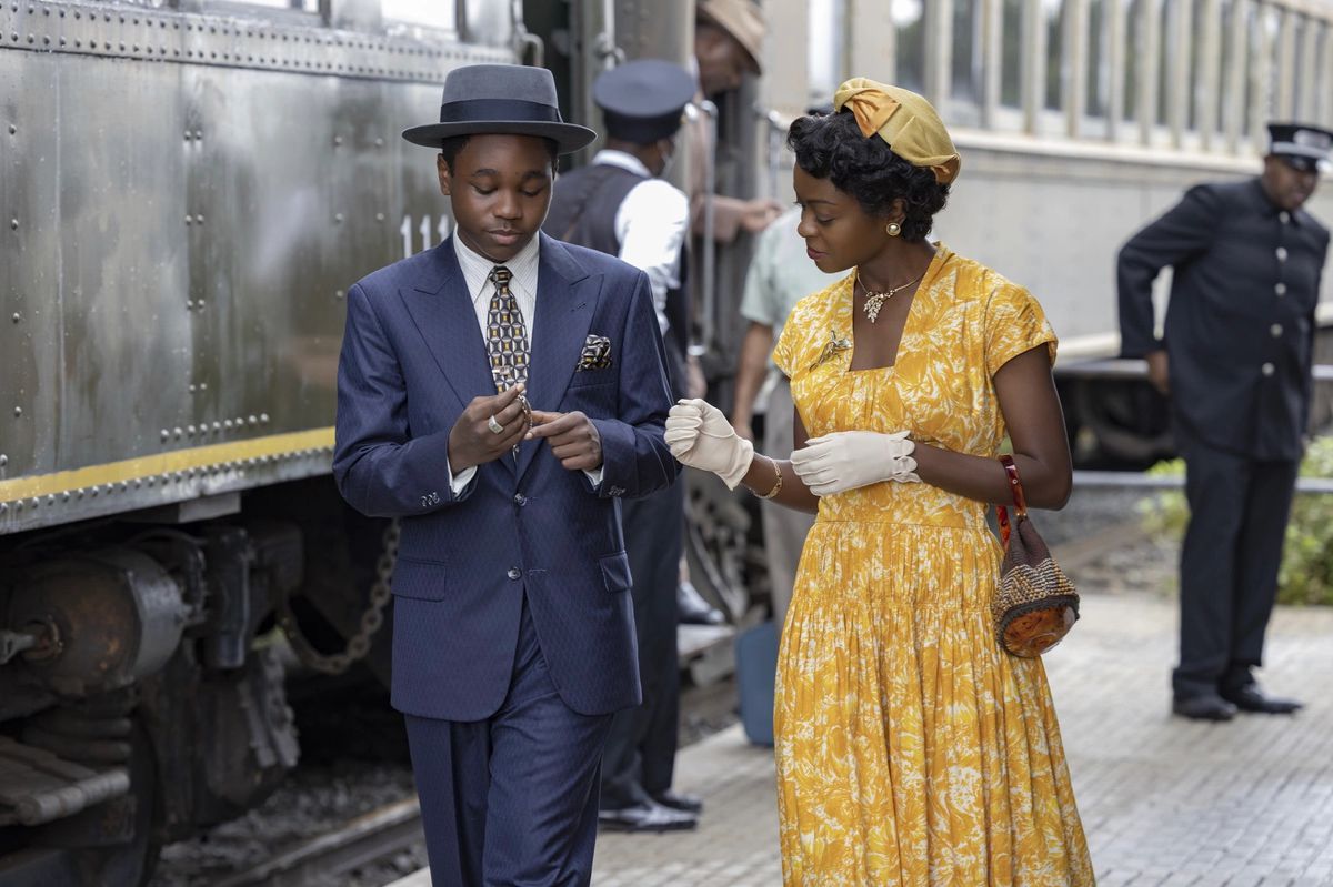 Un garçon en costume bleu marine (Jalyn Hall) se tient à côté d'une femme en robe jaune (Danielle Deadwyler) à côté d'une locomotive.