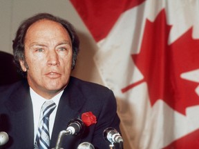 Le premier ministre canadien Pierre Elliott Trudeau, portant une rose à la boutonnière, s'adresse aux médias le 23 octobre 1974 à Paris devant un drapeau canadien.