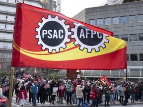 Un drapeau flotte alors que des membres de l'Alliance de la fonction publique du Canada marchent sur la ligne de piquetage devant les édifices gouvernementaux, le vendredi 21 avril 2023 à Gatineau, au Québec.