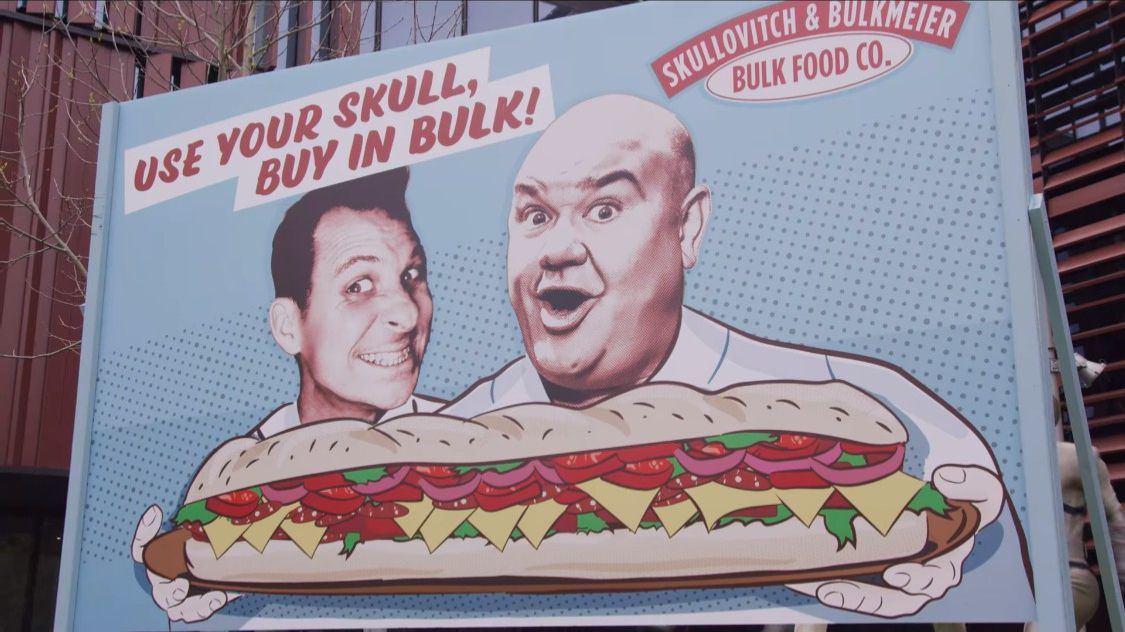 Une photo d'un panneau d'affichage avec deux hommes derrière un sandwich de dessin animé.  Au-dessus d'eux, il est écrit 