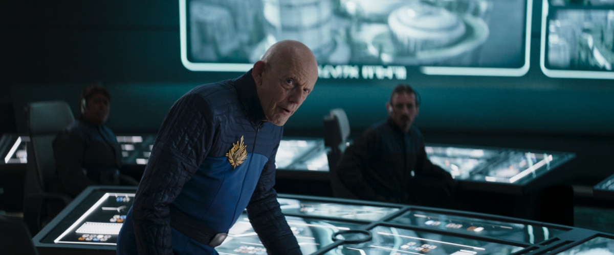 Christopher Lloyd dans The Mandalorian portant un uniforme de sécurité Plazir-15 et penché sur une console de boutons 