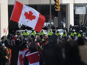 Une personne agite un drapeau canadien alors que des policiers à cheval et un véhicule de police blindé sont positionnés devant des manifestants, le 22e jour d'une manifestation contre les mesures COVID-19 qui s'est transformée en une manifestation antigouvernementale plus large, à Ottawa, le 22 février 2020. 18, 2022.
