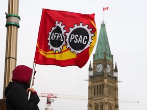 Un travailleur de l'AFPC tient un drapeau sur une ligne de piquetage à Ottawa, le mercredi 19 avril 2023. Le plus grand syndicat de la fonction publique fédérale du Canada et le gouvernement fédéral restent à la table de négociation alors que la grève des travailleurs et les interruptions de service commencent à se faire sentir dans tout le pays.