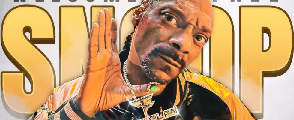 Snoop Dogg holds up a FaZe Clan necklace while posing in front of a sign reading