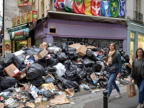 Des piétons passent devant des poubelles pleines dans le 5e arrondissement de Paris alors que les éboueurs font grève contre la réforme des retraites, laissant de nombreuses rues de la capitale remplies de déchets puants le 17 mars 2023.