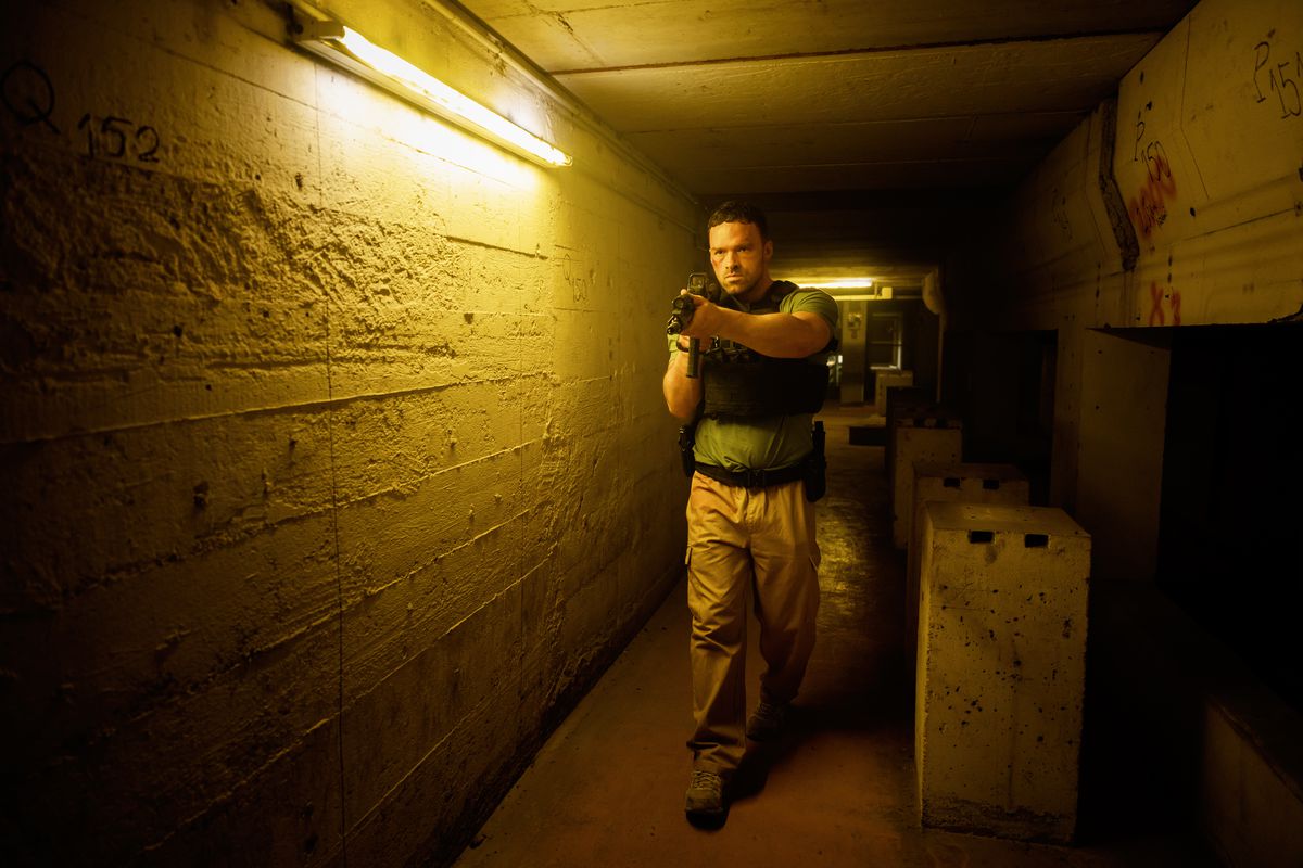 Alban Lenoir traverse un long couloir tout en tenant un fusil d'assaut dans AKA.