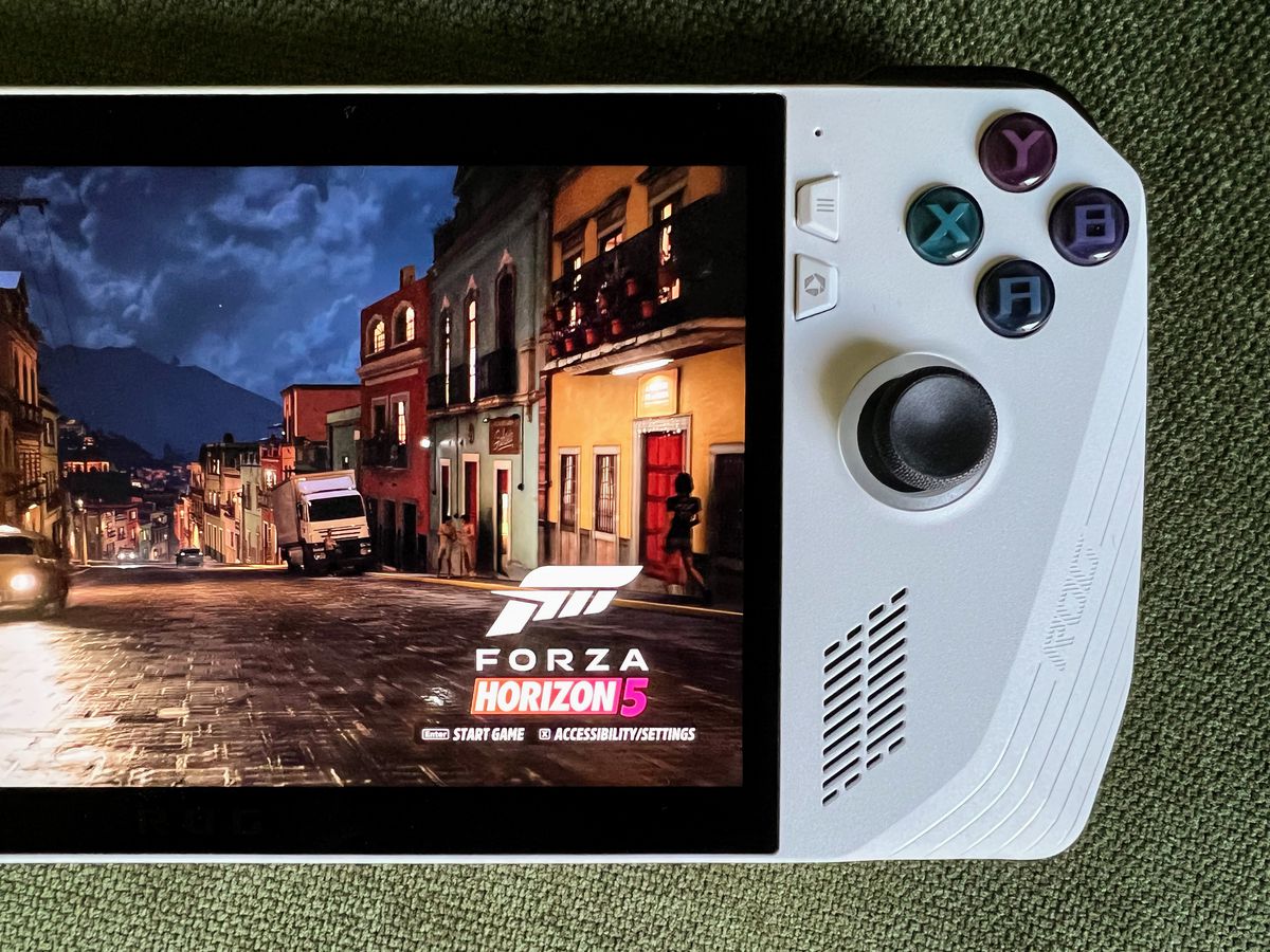 une scène de rue pluvieuse dans Forza Horizon 5 s'exécutant sur un ordinateur de poche de jeu Asus ROG Ally, allongé sur un tissu vert olive, sur une photo aérienne en gros plan du côté droit de l'appareil