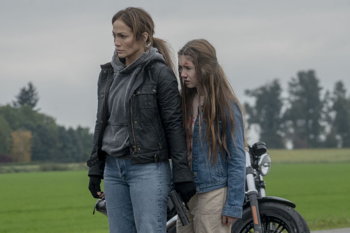 Jennifer Lopez, vêtue d'une veste en cuir, se tient protectrice devant Lucy Paez, devant une moto, dans The Mother.