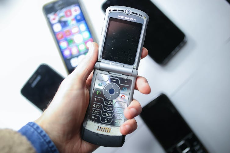 Une main tenant un téléphone portable à clapet au-dessus d'une table recouverte d'un assortiment de smartphones.