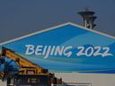 Dans cette photographie d'archive prise le 4 janvier 2022, des ouvriers installent une banderole sur l'enseigne d'un bâtiment du parc olympique de Pékin à Pékin, hôte des Jeux olympiques d'hiver de 2022. 