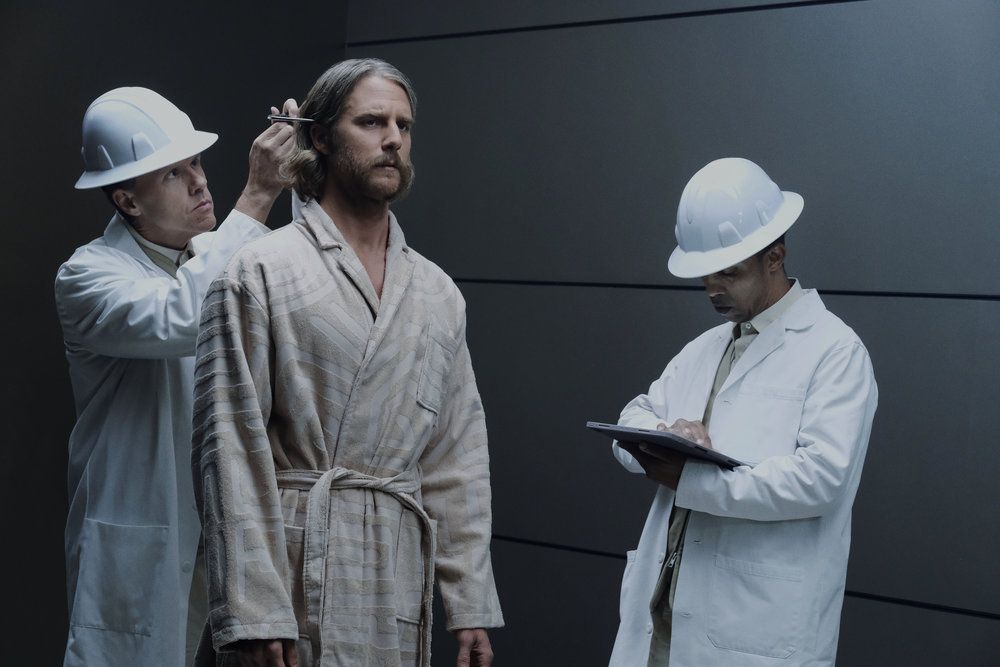 Wiley (Jake McDormand) inspecté par deux hommes portant des blouses de laboratoire et des casques de sécurité dans une image de Mme Davis saison 1