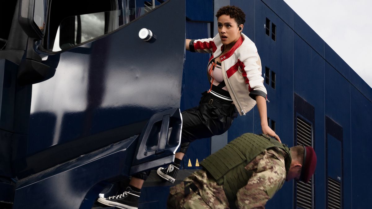 Ramsey (Nathalie Emmanuel) dans Fast X est accrochée à la portière côté conducteur d'un camion de sécurité en mouvement, une main sur un soldat en uniforme qu'elle vient de sortir du camion et qu'elle jette au sol.