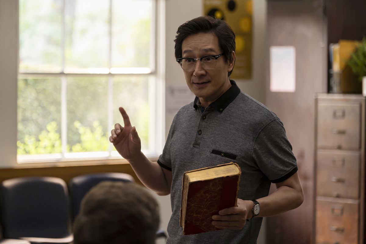 Ke Huy Quan en chinois d'origine américaine.  Il tient un livre à la main et semble enseigner devant une classe.