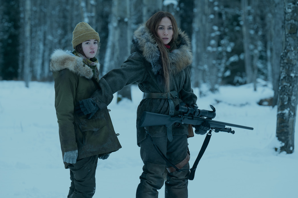 (L, R), Lucy Paez et Jennifer Lopez, qui tient une arme à feu, sont dans les bois hivernaux, dans The Mother