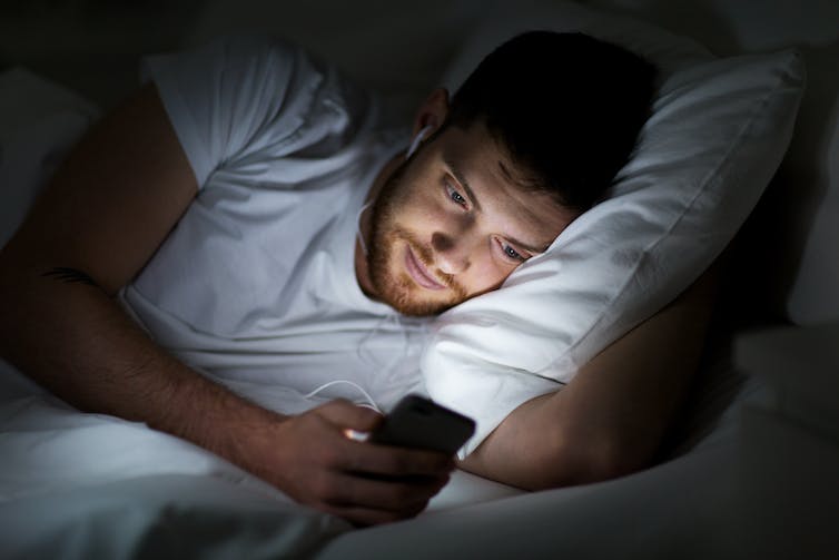 Un homme regarde un smartphone allongé dans son lit