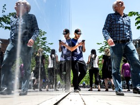 Un jeune homme avec un téléphone portable est mis en miroir avec d'autres piétons à Toronto