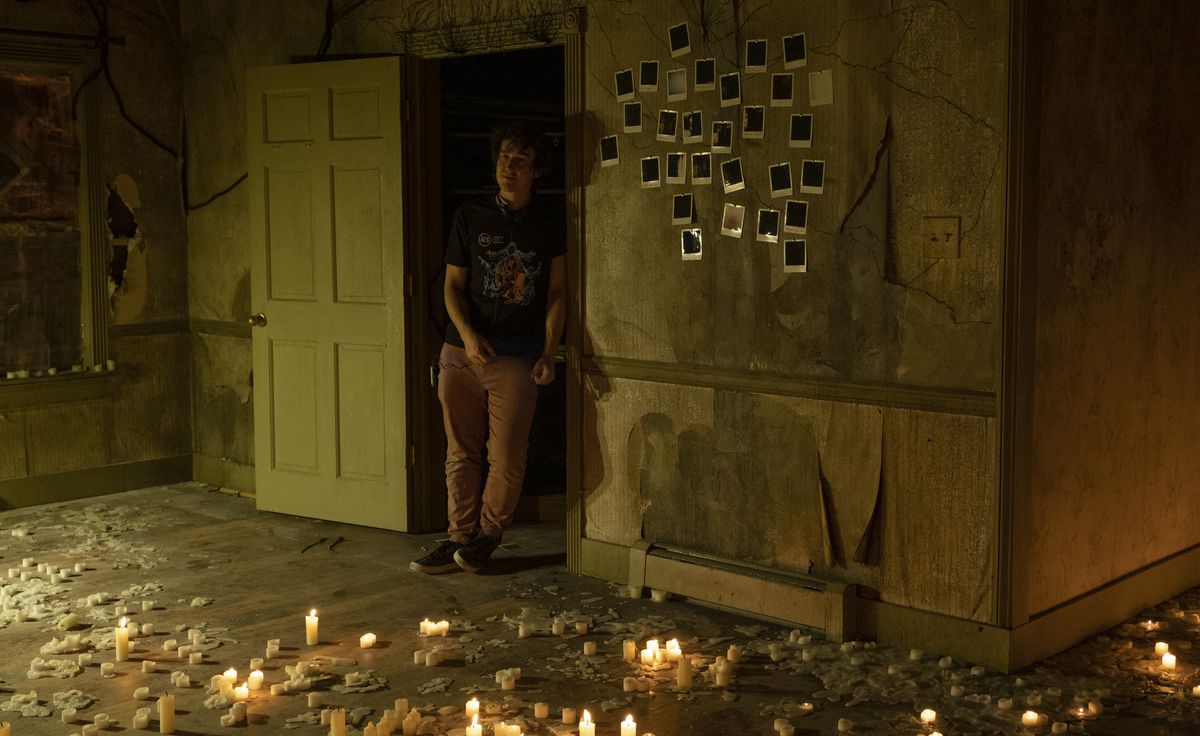 Rob Savage debout dans une maison délabrée avec des polaroids sur le mur éclairés par des bougies alias le tournage de The Boogeyman