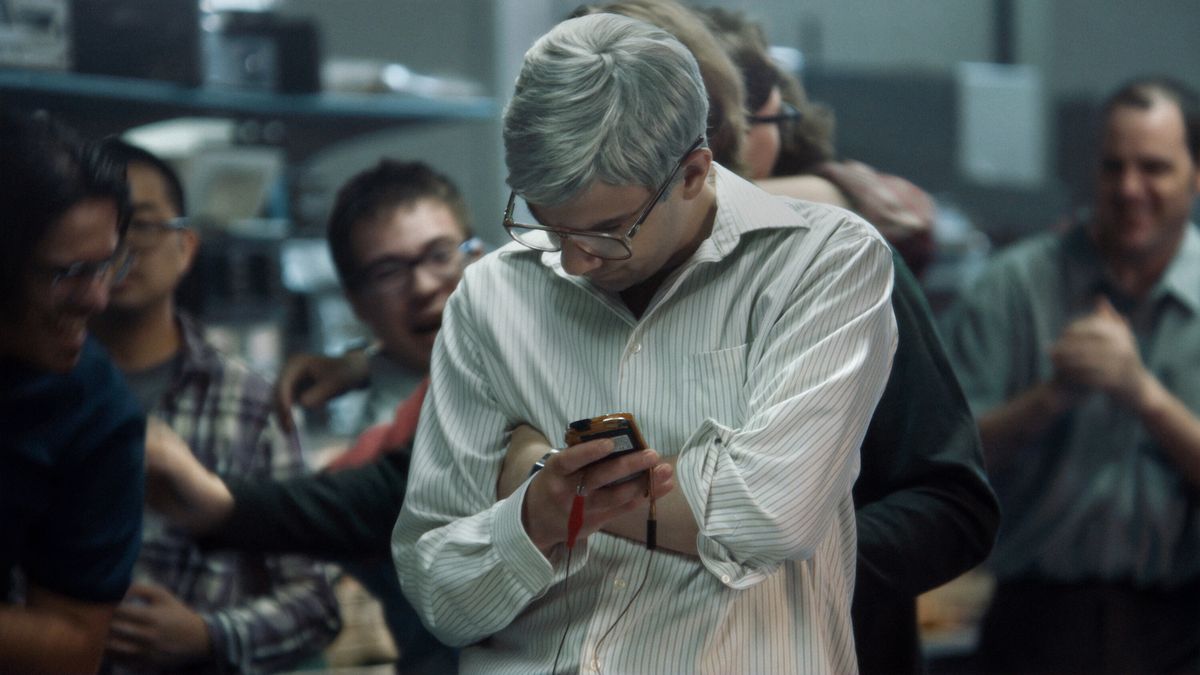 Jay Baruchel en tant qu'homme aux cheveux grisonnants et à lunettes (Mike Lazaridis) tenant un prototype d'appareil BlackBerry dans BlackBerry.