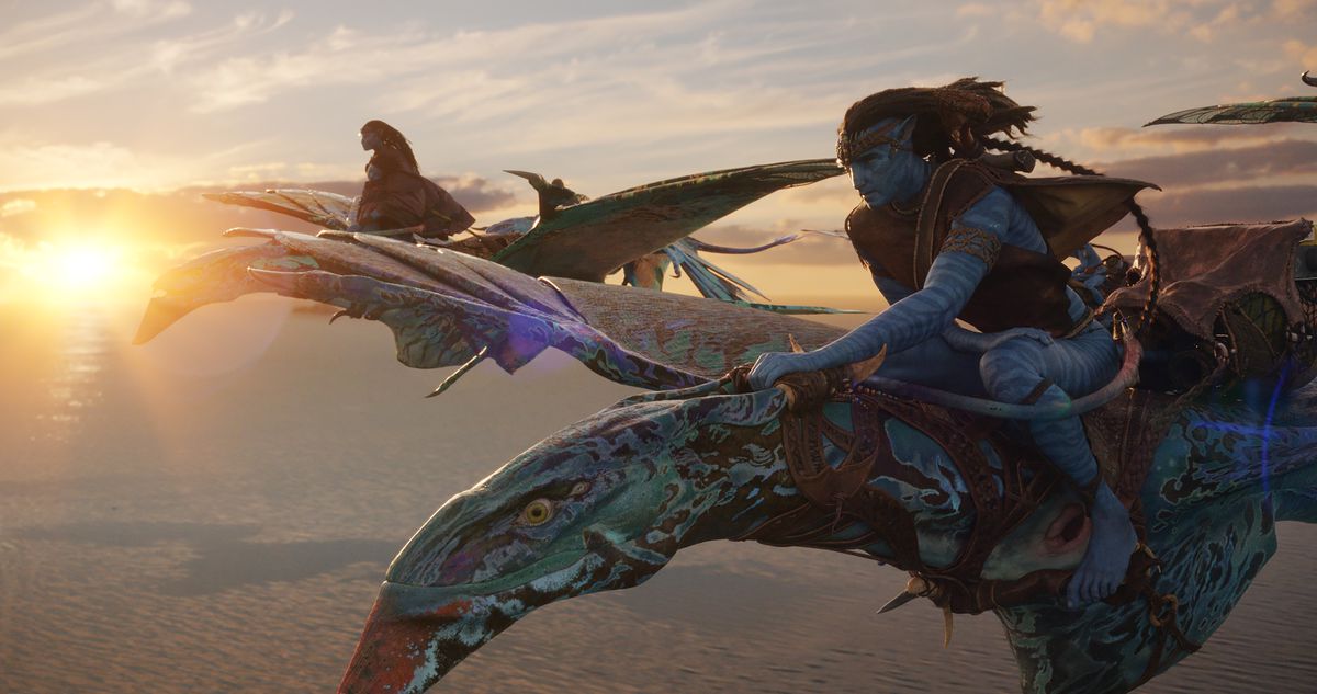 Les compagnons Na'vi Neytiri (Zoe Saldaña) et Jake (Sam Worthington) volent sur leurs montures banshee bleues tachetées au-dessus des nuages ​​avec un coucher de soleil derrière eux dans Avatar: The Way of Water