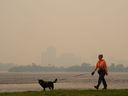 Une femme promène son chien le long de la rivière des Outaouais à Ottawa alors que la fumée des incendies de forêt obscurcit Gatineau, au Québec, au loin le mardi 6 juin 2023.