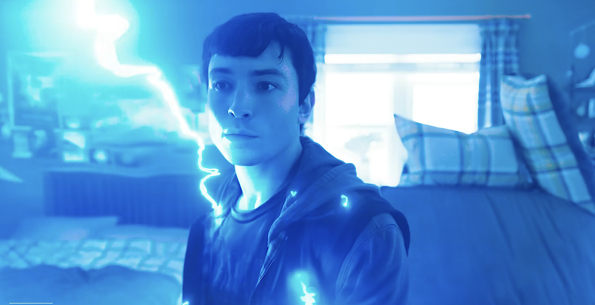 Flash (Ezra Miller), vêtu d'un t-shirt et d'un sweat à capuche, est assis dans la chambre de son enfance alors que des éclairs bleus crépitent à travers son corps dans The Flash