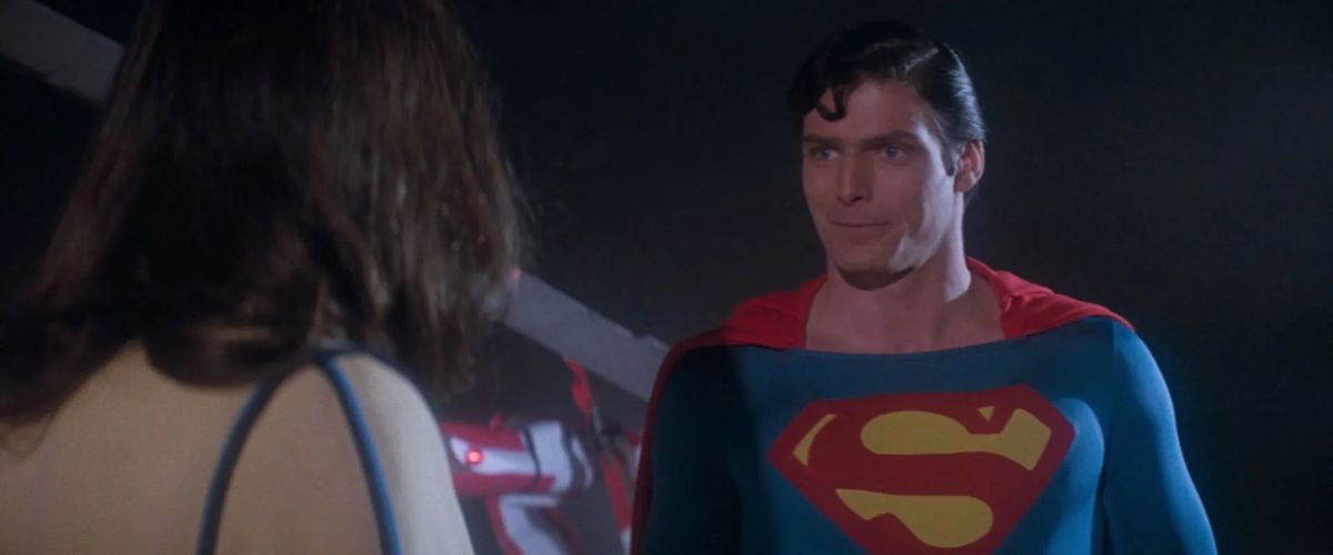 Christopher Reeve dans le rôle de Superman affronte Margot Kidder dans le rôle de Lois Lane, avec un petit sourire décalé sur son visage dans Superman (1978).