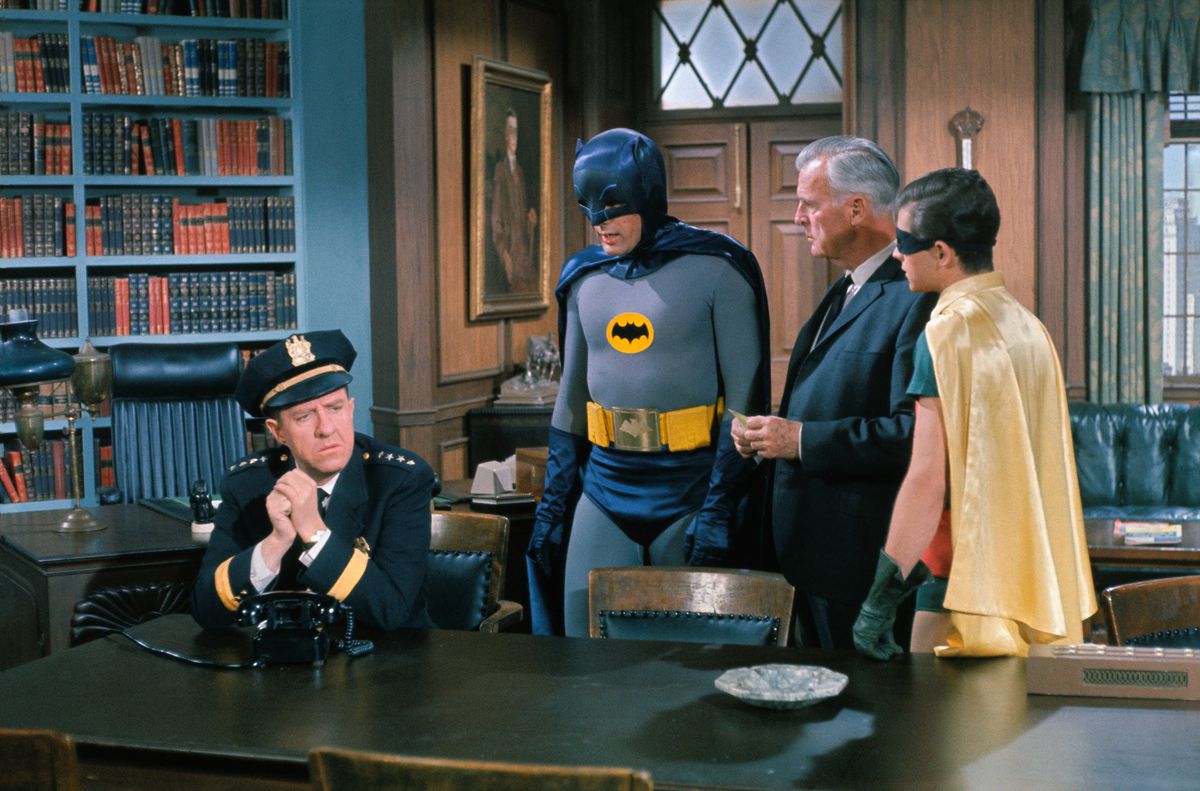 Adam West et Burt Ward dans le rôle de Batman et Robin, se tiennent dans une bibliothèque et discutent avec le commissaire Gordon et le chef O'Hara dans Batman (1966).