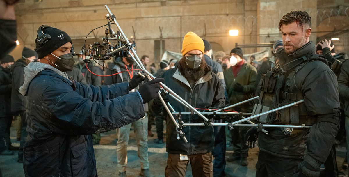 Le réalisateur Sam Hargrave et un caméraman attachent une caméra à la poitrine de Chris Hemsworth avec une série de perches argentées articulées télescopiques pour une partie de la première séquence d'Extraction 2