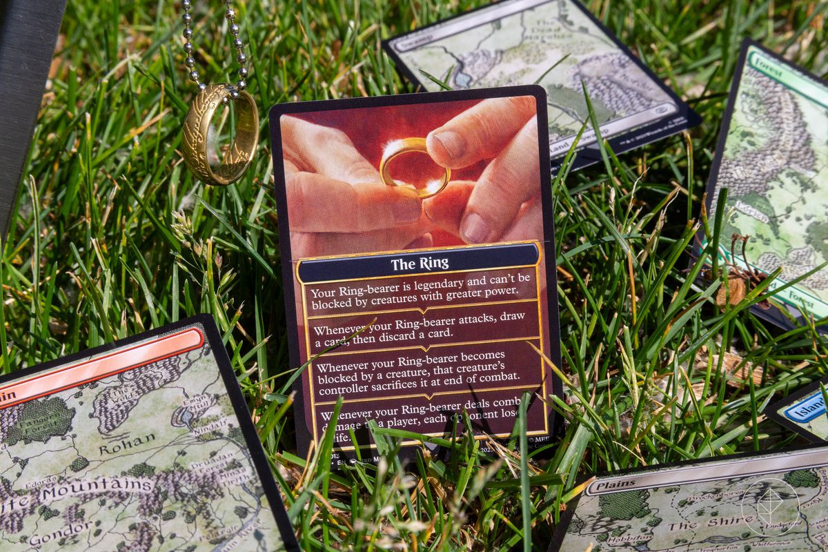 Une image montrant plusieurs cartes Magic: the Gathering posées sur l'herbe.  Celui qui est mis au point est L'Anneau de l'ensemble Contes de la Terre du Milieu.