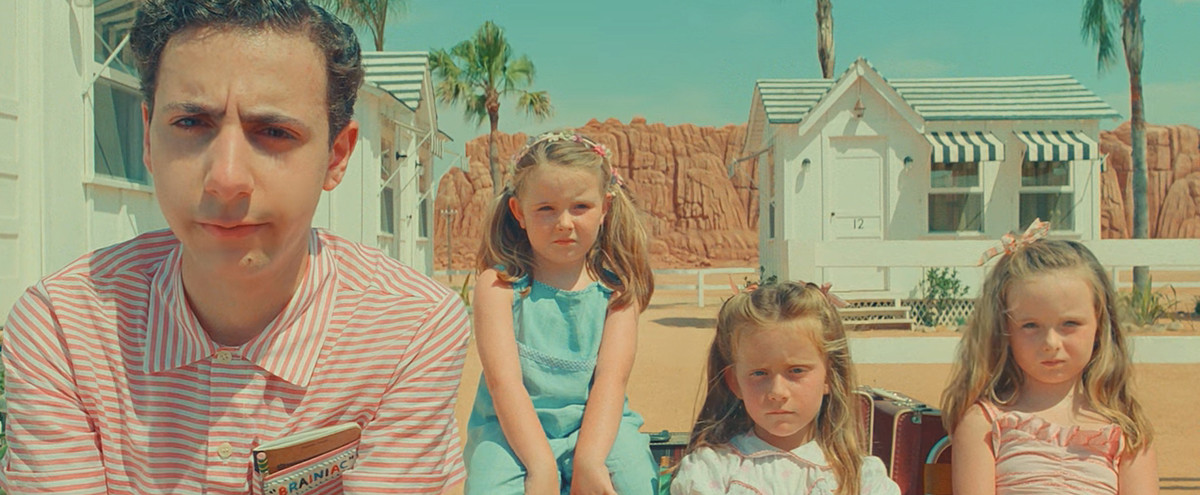 l'adolescent Woodrow Steenbeck (Jake Ryan) et ses frères et sœurs triplés, trois jeunes filles, sont assis devant un motel pastel et blanc dans le désert de Wes Anderson's Asteroid City