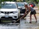 Inondations sur la Première Avenue à Ottawa lundi après une violente tempête de pluie.  Kim Saravanamuttoo essaie de dégager sa grille d'égout pour maintenir le niveau d'eau bas dans sa rue.   