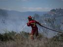 Un pompier dirige l'eau sur un feu d'herbe qui brûle sur une superficie derrière une propriété résidentielle à Kamloops, en Colombie-Britannique, le lundi 5 juin 2023. Les néo-démocrates demandent au gouvernement fédéral d'augmenter le crédit d'impôt pour les pompiers volontaires alors qu'ils combattent les incendies de forêt qui font rage à travers le pays.  LA PRESSE CANADIENNE/Darryl Dyck