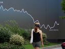 Un piéton passe devant un écran géant montrant un graphique boursier, à Shanghai, en Chine.