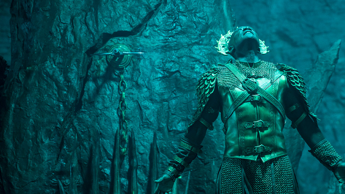 Peter Mensah dans le rôle de l'archange Michel, regardant une source de lumière inconnue avec un mur de pierre en arrière-plan dans The Devil Conspiracy.