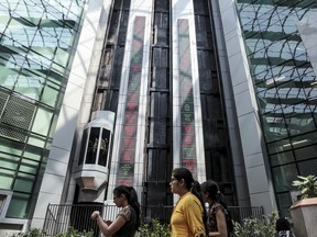 Des employés passent devant des téléscripteurs électroniques qui indiquent les derniers chiffres boursiers à l'intérieur de l'atrium de la Bourse nationale de Mumbai, en Inde.