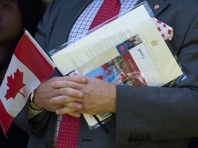 Un nouveau Canadien tient un drapeau canadien, son certificat de citoyenneté et une lettre signée par le premier ministre Justin Trudeau alors qu'il chante O Canada après être devenu citoyen canadien, lors d'une cérémonie spéciale de citoyenneté pour la fête du Canada à West Vancouver le lundi 1er juillet 2019.