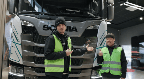 Two men standing in front of a big truck and smiling.