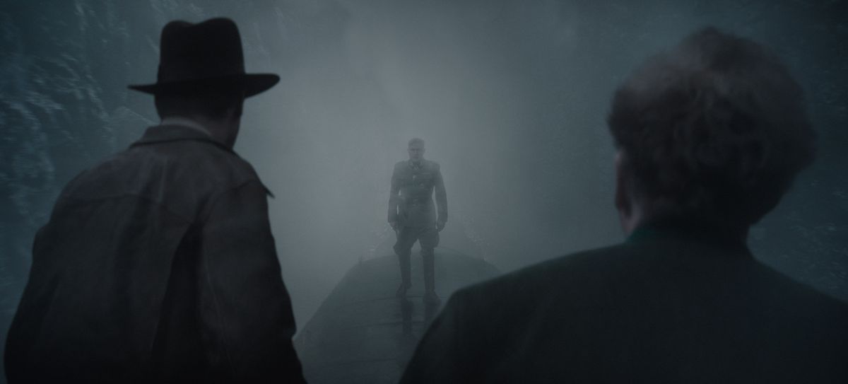 Indiana Jones (à gauche) et Basil Shaw (à droite), dos au spectateur, affrontent le méchant Jurgen Voller, se découpant dans la brume, au sommet d'un train en marche.