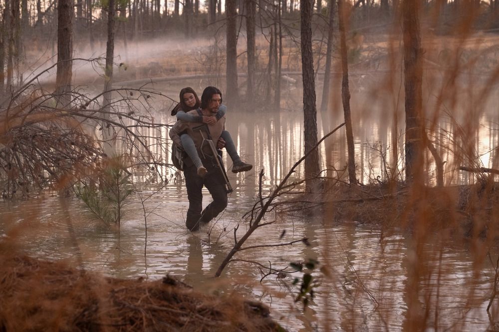 Mills (Adam Driver) transportant Koa (Ariana Greenblatt) à travers un marais entouré de feuillage en 65.
