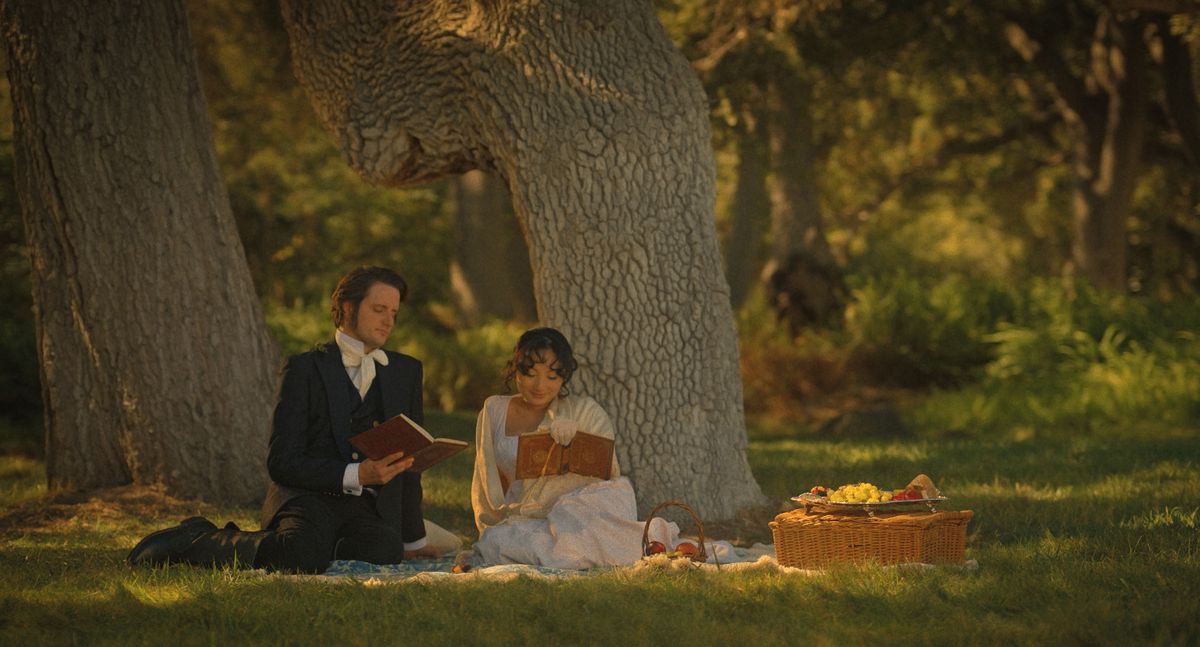 Une mariée et un marié en robe d'époque Jane Austen lisent sur une couverture de pique-nique dans les bois dans The Afterparty saison 2