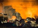 De la fumée et du feu s'élèvent au-dessus des wagons alors que les pompiers inspectent la zone après qu'un train transportant du pétrole brut a déraillé et explosé dans la ville de Lac-Mégantic le 6 juillet 2013. 