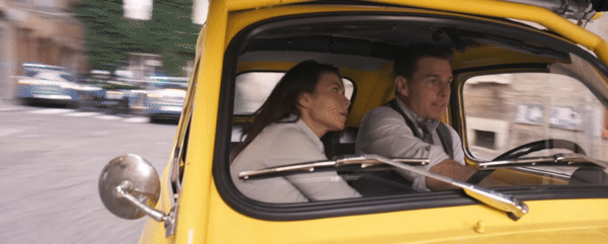 Ethan Hunt (Tom Cruise) et Grace (Hayley Atwell) sont assis menottés dans une fiat jaune alors qu'Ethan fait tourner le volant dans une rue de Rome