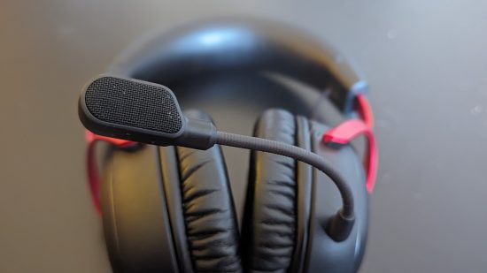 Revue HyperX Cloud 3 : un casque noir et rouge est assis sur une table noire, avec le microphone net près de la caméra.