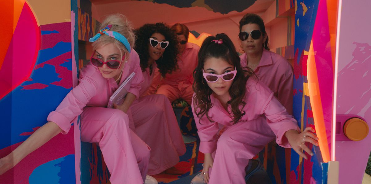 L'arrière d'une fourgonnette peinte au néon criard s'ouvre pour révéler quatre femmes portant des combinaisons rose poudré assorties et des lunettes de soleil à monture rose non assorties : Barbie (Margot Robbie), également Barbie (Alexandra Shipp), Sasha (Ariana Greenblatt), et Gloria (America Ferrera), dans le film d'action en direct 2023 Barbie