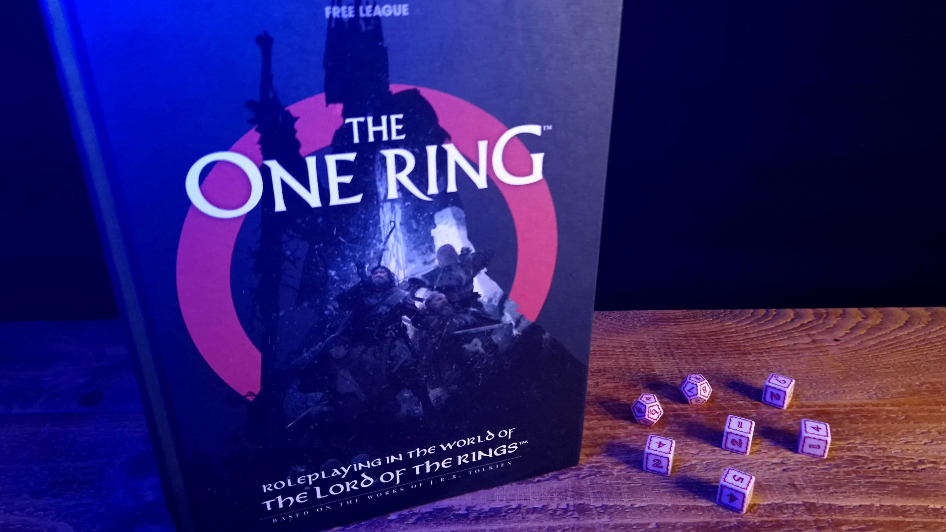 Le One Ring Core Rulebook et les dés sur une table en bois, sur un fond sombre