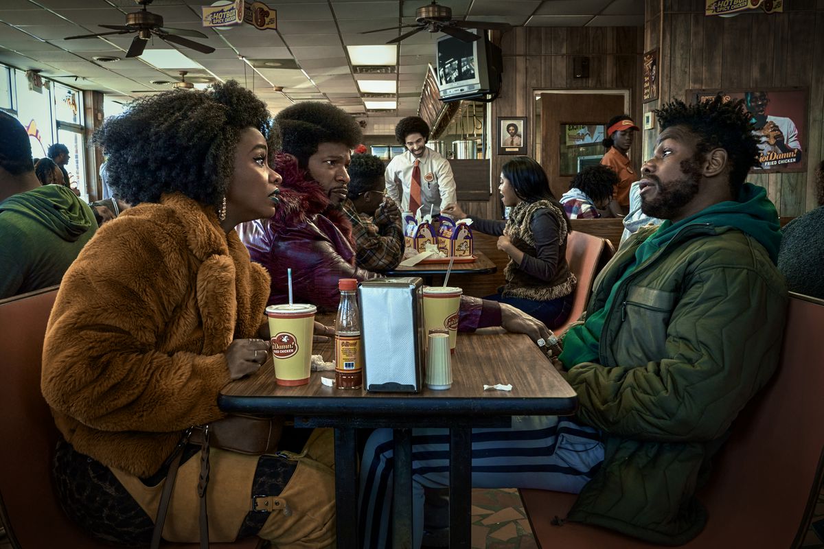 (De gauche à droite) Teyonah Parris comme Yo-Yo, Jamie Foxx (producteur) comme Slick Charles et John Boyega comme Fontaine assis l'un en face de l'autre dans un restaurant de restauration rapide à ils ont cloné Tyrone.