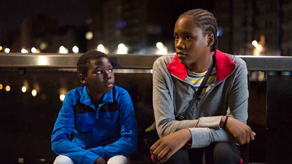 Un jeune garçon (Pablo Schils) et une jeune femme (Mbundu Joely) assis sur un banc la nuit à Tori et Lokita.