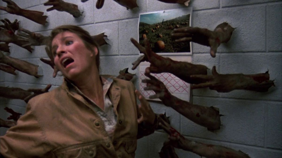 Des dizaines de bras de zombies ont éclaté à travers un mur alors qu'une femme hurle dans Day of the Dead.
