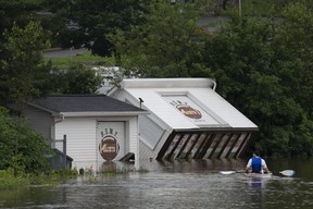 Des bâtiments sont vus renversés sur une berge alors qu'un homme pagaie en kayak dans les eaux de crue à la suite d'un événement pluvieux majeur à Halifax