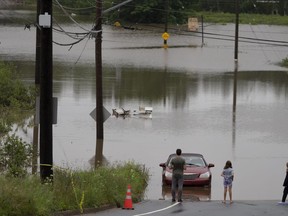 Des gens se tiennent au bord des eaux de crue alors que des véhicules sont vus abandonnés dans l'eau à la suite d'un événement pluvieux majeur à Halifax le samedi 22 juillet 2023.